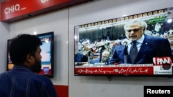 یک فروشنده جریان پیشنهاد بودجهٔ دولتی توسط وزیر مالیهٔ پاکستان در پارلمان این کشور را تماشا دارد