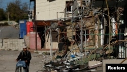 FILE - A man walks with his bicycle through a shopping street destroyed by Russian strikes in the town of Kupiansk, Ukraine, Oct. 18, 2022. 