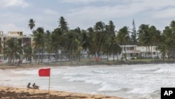 Tourists sit on La Pared beach as Tropical Storm Ernesto passes by Luquillo, Puerto Rico, Aug. 13, 2024. 