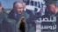A woman passes a billboard showing Russian President Vladimir Putin in Damascus, Monday, March 7, 2022. The Arabic poster reads "The victory for Russia." (Omar Sanadiki/AP)