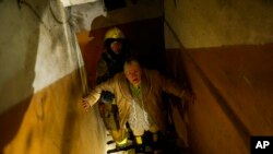 A woman is helped by a Ukrainian firefighter to leave a shelter after Russian shelling in Kharkiv, Oct. 8, 2022. A series of explosions have rocked the city, sending towering plumes of illuminated smoke into the sky and triggering a series of secondary ex
