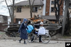 Local civilians walk past a tank in an area controlled by Russian-backed separatist forces in Mariupol, Ukraine, Tuesday, April 19, 2022.