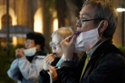 People with masks blow whistles to representing a whistleblower during a vigil for Chinese doctor Li Wenliang, in Hong Kong, Feb. 7, 2020.