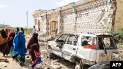 Sejumlah perempuan berjalan melintas di depan mobil dan rumah yang rusak akibat ledakan bom oleh militan al-Shabab di Mogadishu, Somalia, 16 Februari 2022. (Foto: Hassan Ali Elmi/AFP)