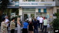 មនុស្ស​ម្នា​ឈរ​តំរង់​ជួរ​គ្នា​ដើម្បី​ប្រើប្រាស់​ម៉ាស៊ីន​អេធីអឹម (ATM) នៅ​ខាង​ក្រៅ​ធនាគារ​ដែល​បិទ​ទ្វារ​ នៅ​ក្បែរ​ស្លាក​សញ្ញា​នៅ​លើ​ដើម​ឈើ​ ដែល​សរសេរ​ថា «ទេ» ក្នុង​ក្រុង​អាថែន (Athens) កាលពី​ថ្ងៃទី​៣០ ខែមិថុនា ឆ្នាំ២០១៥។