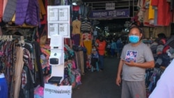 បុរសម្នាក់ពាក់ម៉ាស់ឈរជិតប្រអប់លាងដៃស្វ័យប្រវត្តិមួយ ដែលត្រូវបានដាក់នៅខាងមុខផ្លូវចូលក្នុងផ្សារមួយ ក្នុងរាជធានីភ្នំពេញ កាលពីថ្ងៃទី២៣ ខែកុម្ភៈ ឆ្នាំ២០២១។ (ទុំ ម្លិះ/វីអូអេ)