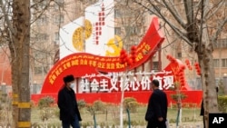 FILE - Residents walk past government propaganda, some of which reads, "Socialist core values," in Hotan in northwestern China's Xinjiang Uyghur Autonomous Region, March 22, 2021.