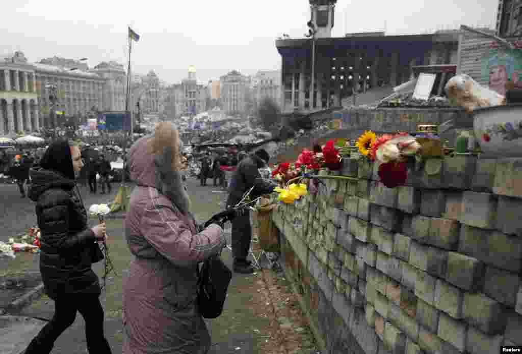 Two women prepare to place flowers on a wall in the Independence Square in Kyiv.