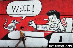 Seorang perempuan berjalan melewati tembok berhias grafiti yang menunjukkan dukungan terhadap gerakan anti korupsi pemerintah di Jakarta, 20 Juli 2010. (Foto: AFP/Bay ISMOYO)