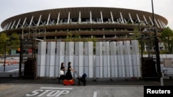Pedestrians wearing protective masks, following the coronavirus disease (COVID-19) outbreak, walk in front of the National Stadium, the main stadium of Tokyo 2020 Olympics and Paralympics in Tokyo, Japan, July 7, 2021. 