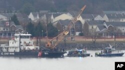 A member of a dive team and a Coast Guard vessel with a crane are pictured as they work near the wreckage of a Black Hawk helicopter in the Potomac River from Ronald Reagan Washington National Airport, Jan. 31, 2025, in Arlington, Va. 