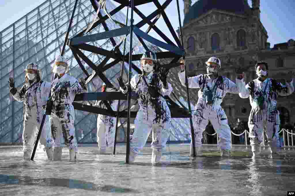 Greenpeace activists wearing the uniform of petroleum workers stand next to a smoking 'oil well tower' in front of The Louvre Museum Pyramid in Paris as they protest against French energy company Total and continued world fossil fuel production and consumption.