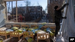 FILE - A man removes a destroyed curtain inside a school damaged among other residential buildings in Kyiv, Ukraine, Friday, March 18, 2022. The Ukrainian government says Russia has shelled more than 1,000 schools, completely destroying 95. (AP Photo/Rodrigo Abd, File)