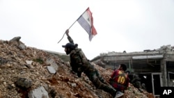 Seorang tentara Suriah menempatkan bendera nasional Suriah saat bertempur dengan pejuang pemberontak timur dari Aleppo, 5 Desember 2016. (AP Photo/Hassan Ammar). 