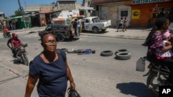 Seorang perempuan berjalan melewati mayat yang tergeletak di jalan di Port-au-Prince, Haiti, pada 20 April 2023. (Foto: AP/Odelyn Joseph)