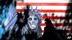 FILE - An Iranian woman walks past graffiti art characterizing the U.S. Statue of Liberty, painted on the wall of the former U.S. Embassy in Tehran, Iran, Sept. 25, 2007. An Iranian-American businessman and his father, who are serving 10-year prison sentences in Iran over their ties to the U.S., have lost a court appeal, a lawyer said Monday, Aug. 28, 2017. 