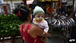 A child is carried next to carts with vegetables and fish being distributed during a 'Donate your extras, take what you need' donation drive aimed at helping low-income households in Yangon, Myanmar, on April 6, 2021.