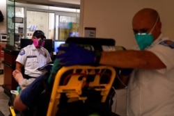 FILE - EMTs Melanie Cristantos, left, and Ryan Schneider wait for a bed to be cleared in an emergency room at Mission Hospital in Mission Viejo, Calif., Dec. 21, 2020.