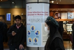 FILE - A woman wearing a face mask passes a Public Health England sign, warning arriving passengers that the coronavirus has been detected in Wuhan in China, at Terminal 4 of London Heathrow Airport in west London on Jan. 28, 2020.