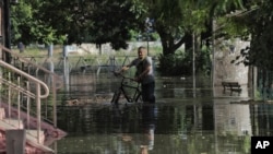 Seorang warga tampak mendorong sepedanya di jalan yang banjir di wilayah Kherson, Ukraina, pada 6 Juni 2023. Banjir hinggap di sejumlah wilayah di Ukraina akibat bendungan Kakhovka yang hancur. (Foto: AP/Nina Lyashonok)