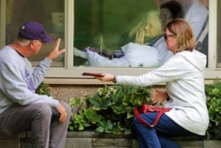FILE - Judie Shape, center, blows a kiss to her son-in-law as her daughter looks on, as they visit on the phone and look at each other through a window at the Life Care Center in Kirkland, Wash., March 11, 2020.