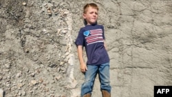 This undated handout picture provided by Giant Screen Films shows Liam Fisher lying next to his discovery - the femur and tibia of a juvenile T. rex in Marmarth, North Dakota. (Photo by Handout / Giant Screen Films / AFP)