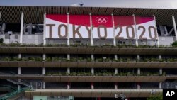 FILE - Workers walk through the front entrance of National Stadium, June 23, 2021, in one month before the opening of the Tokyo Olympic Games.