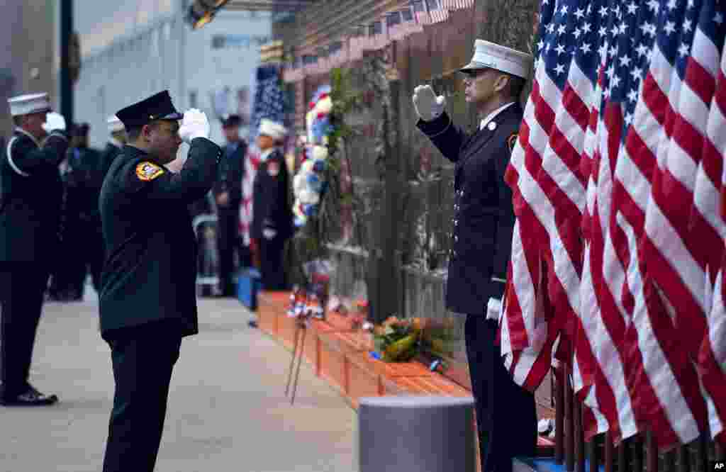 New York City firefighters salute in front of a memorial outside a firehouse adjacent to One World Trade Center and the 9/11 Memorial site in New York, Sept. 11, 2018.