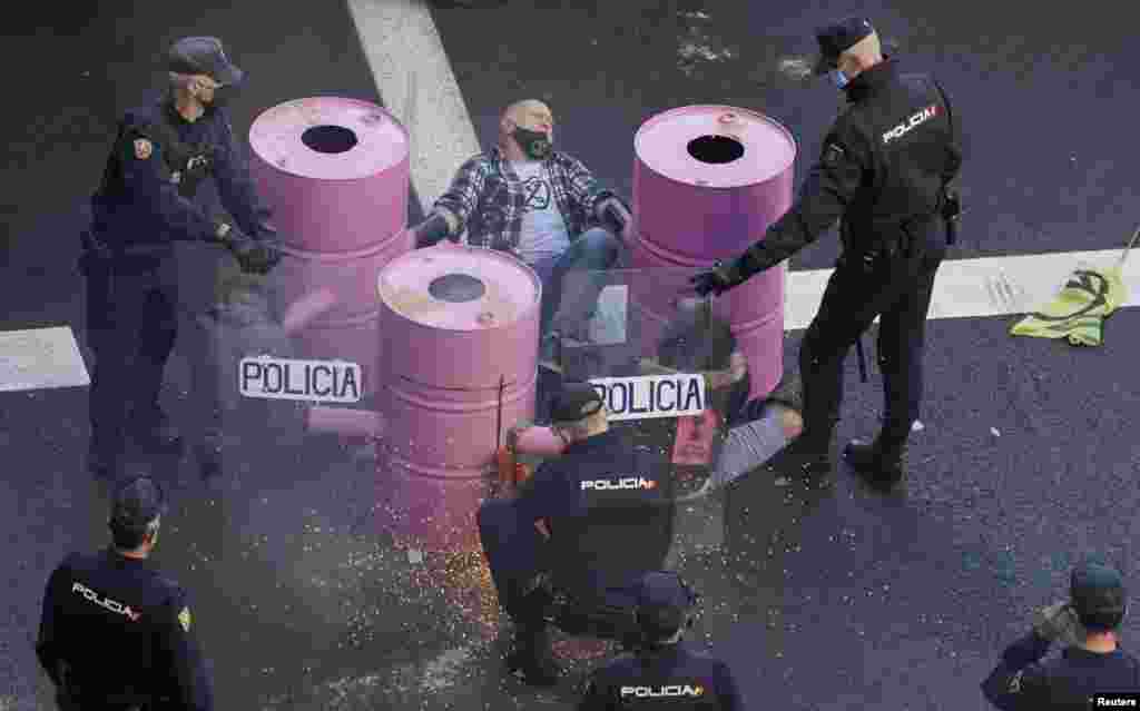 A Spanish police officer uses a radial saw to cut a barrel and remove a climate activist from the road during a protest by Extinction Rebellion against the COP26 summit in Madrid, Spain.