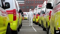 Radnik u zaštitnom odijelu pored vozila za prevoz pacijenata oboljelih od koronavirusa u Južnoj Koreji