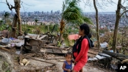 Alona Nacua, right, stands with her son as she looks at their damaged house due to Typhoon Rai in Cebu city, central Philippines on Christmas Day, Dec. 25, 2021. Nacua said she and her husband managed to receive rice and four small cans of sardines and co
