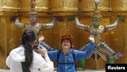 FILE - A Chinese tourist strikes a similar pose to statues as they visit the Grand Palace in Bangkok.